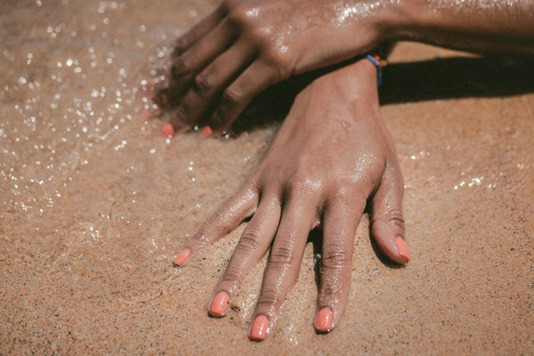 Hands With Orange Nail Polish on Wet Sand at the Beach