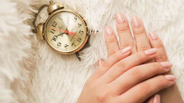 hand showing neutral dip powder nails next to a retro alarm clock