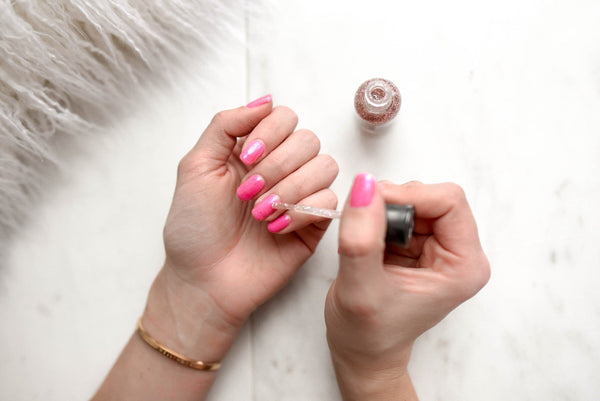 Person applying shimmer gel polish on pink nails at home