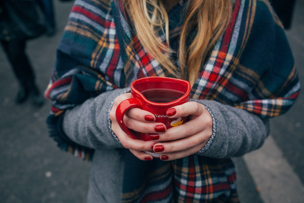 Woman holding red heart shaped mug with red nails
