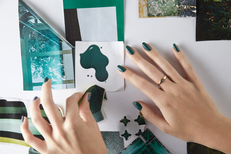 Hands with dark green nails pinning photos to a board